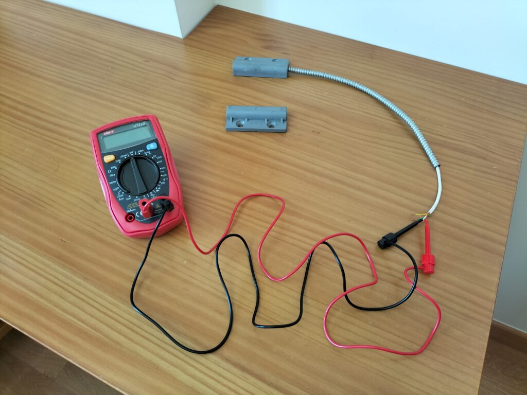 Multímetro conectado a los terminales de un detector magnético (reed switch)